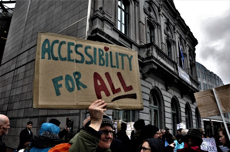 Φωτογραφία από διαδήλωση στις Βρυξέλλες για την προσβασιμότητα- διαδηλωτής κρατάει αυτοσχέδιο πλακάτ που αναγράφει "Accessiblity for All", Προσβασιμότητα για όλους